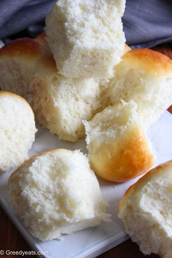 Freshly baked dinner rolls with golden tops kept on a white marble board.