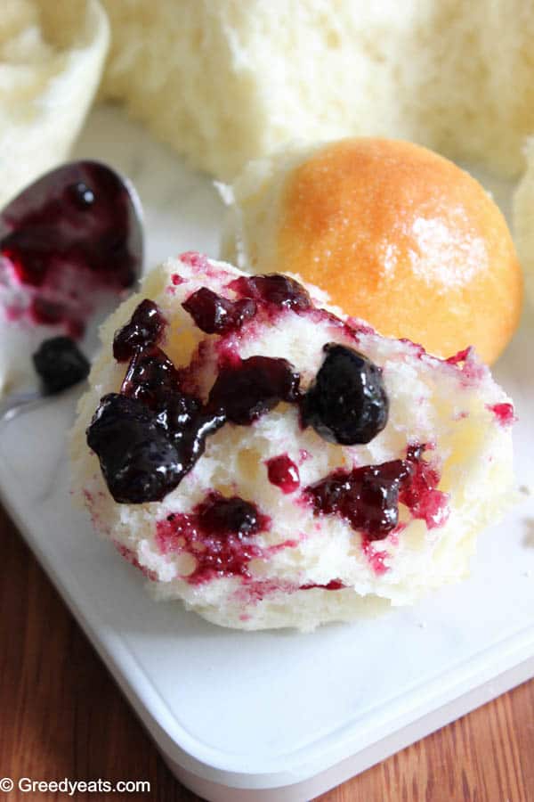 A soft and fluffy chunk of dinner roll slathered with blueberry jam.