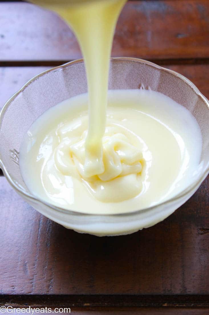 Thick and rich homemade sweetened condensed milk dripping in a glass bowl.