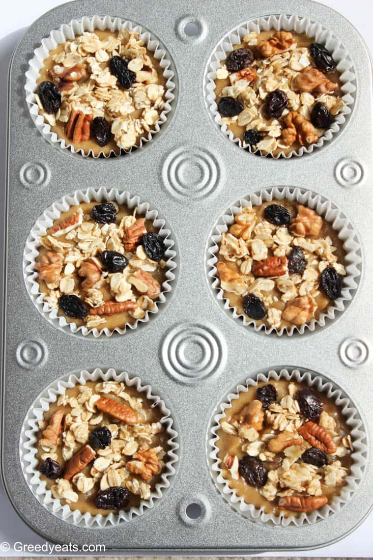 Banana muffins batter poured in liners and topped with oats, nuts and raisins.
