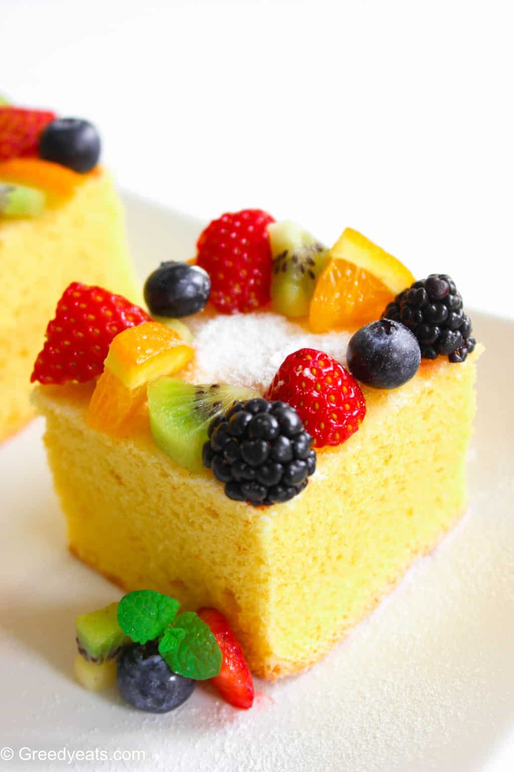 A slice of fluffy lemon cake topped with confectioners' sugar and fresh fruit toppings. 