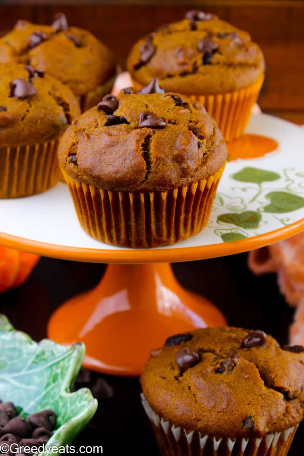 Tall and Fluffy Pumpkin Muffins with melty chocolate chips in an orange wrapper.