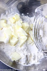 Mixing cold butter cubes into flour for biscuit dough.