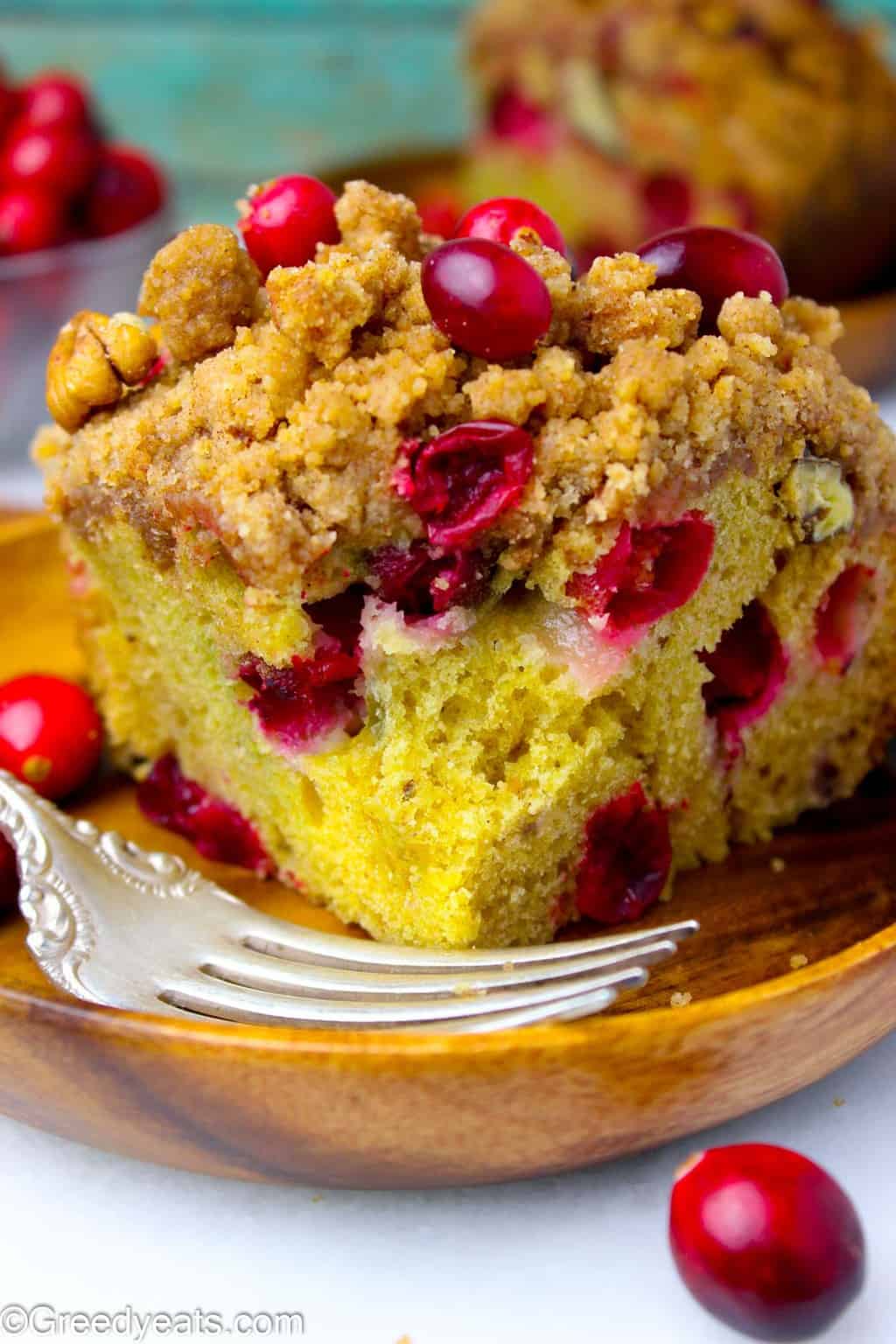 Soft and Buttery orange flavored Cranberry Coffee Cake slice on wooden plate.