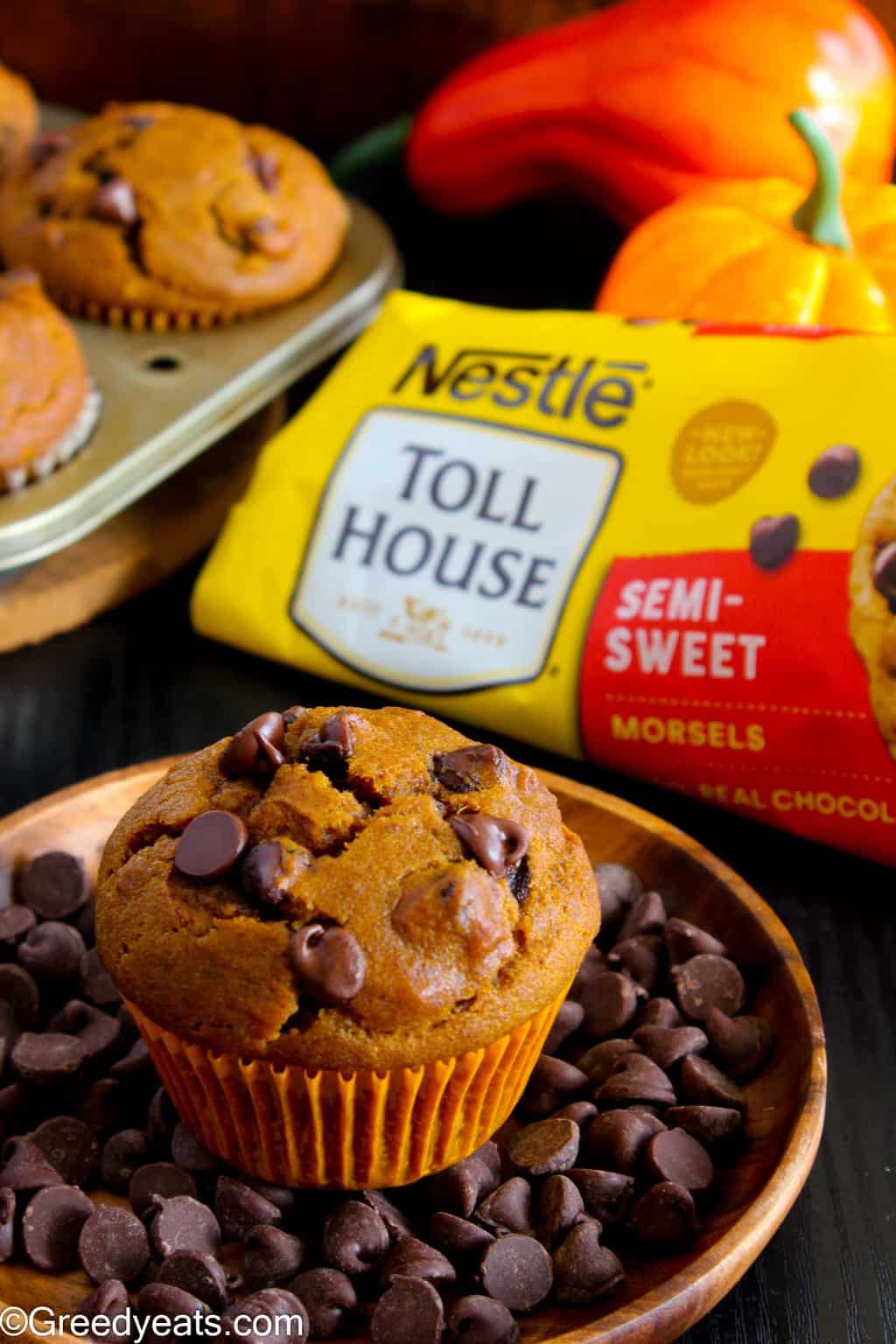 Pumpkin muffins dotted with gooey semi sweet chocolate chips, on a wooden plate.