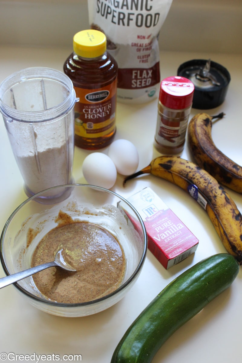 Ingredients like banana, zucchini, almond butter, eggs, oats flour and honey for zucchini bread.