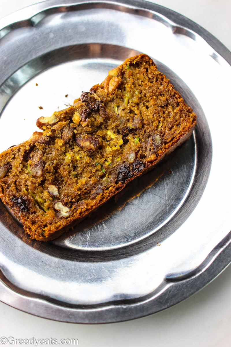 A slice of moist and flavor packed zucchini bread kept on a steel plate.