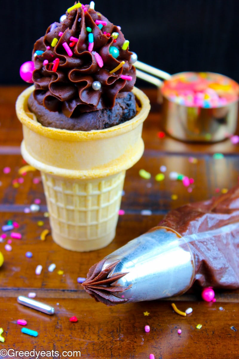 Chocolate frosting in a piping bag and a frosted Ice cream cupcake cone. 
