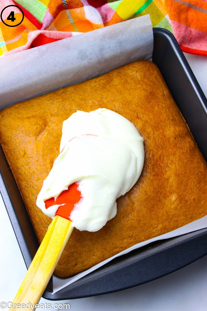 Freshly baked and cooled pumpkin bars getting topped with Cream Cheese Frosting.