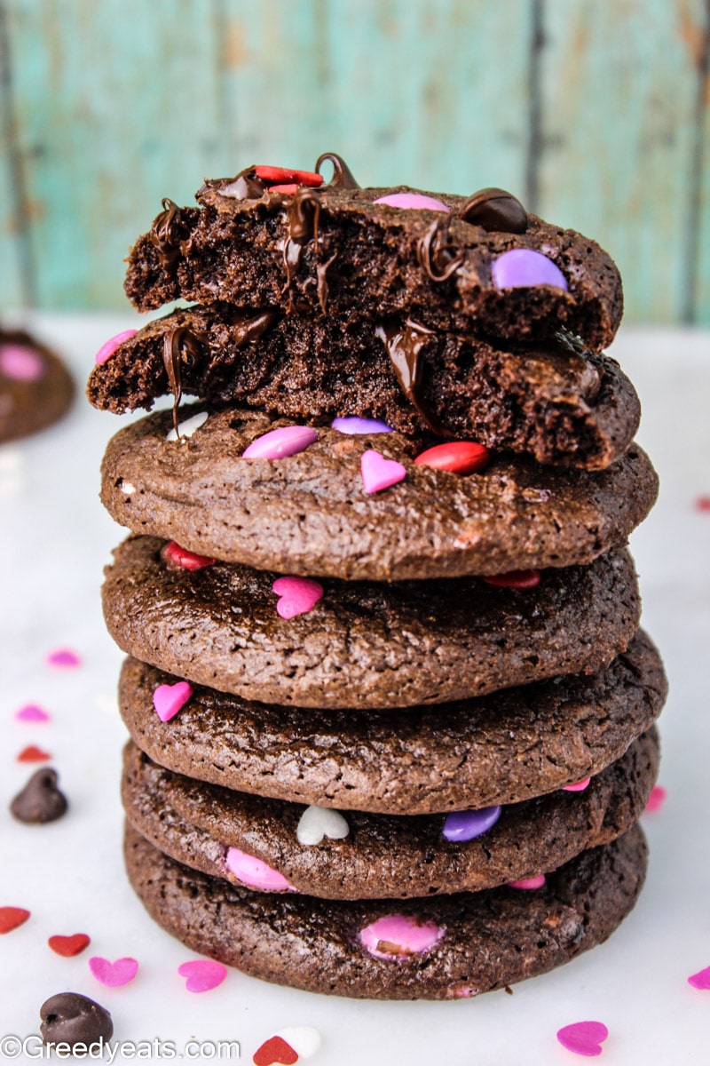 Chocolate m&m cookies dotted with m&ms and pink hearts stacked on a white board.