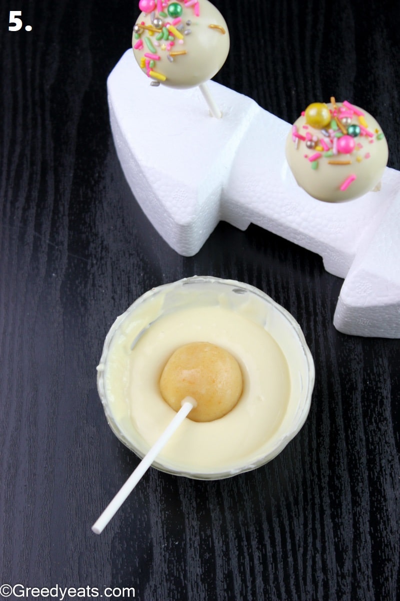 Dipping vanilla cake pops in white chocolate and sticking them on styrofoam to set.