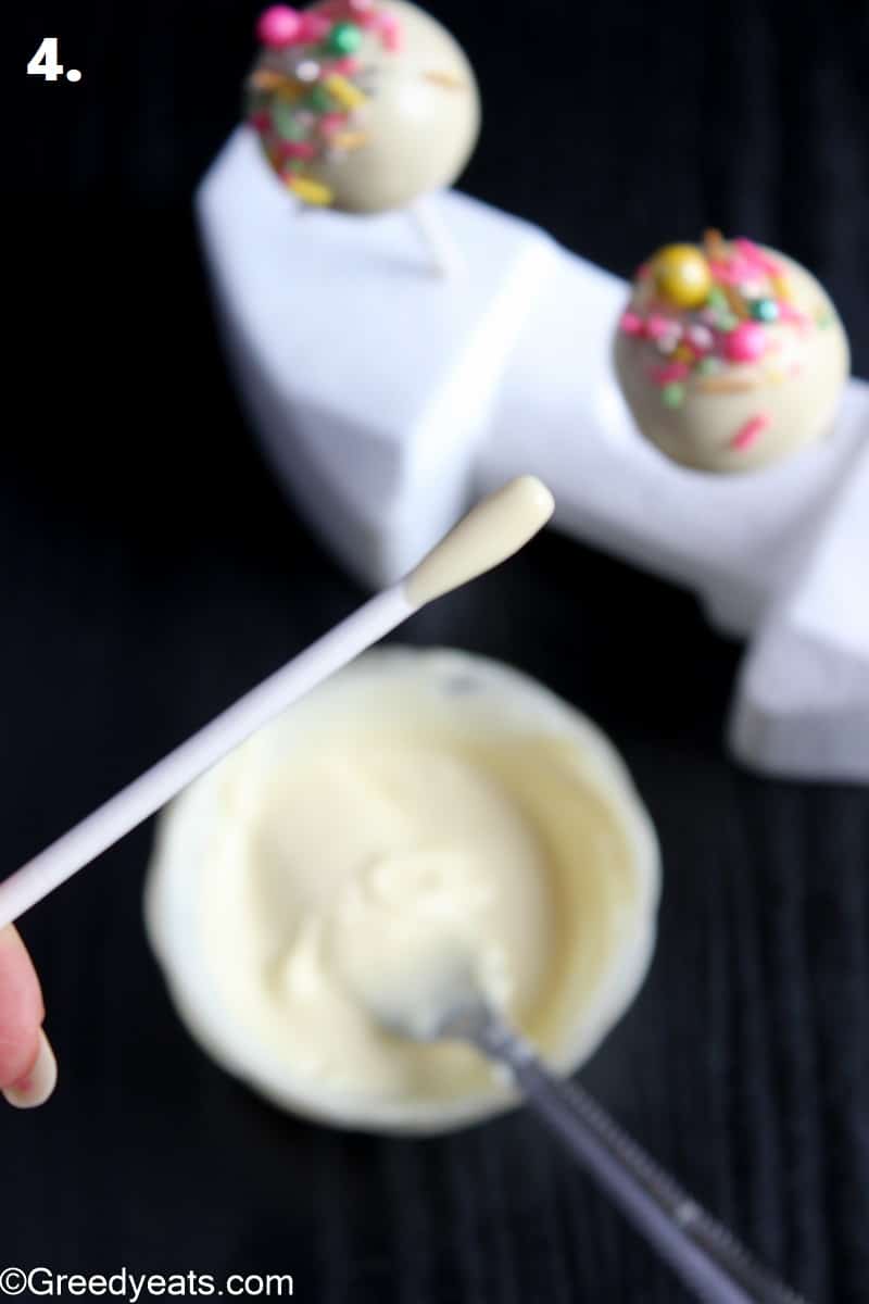 Dipping lollipop stick in melted white chocolate before pressing on cake pop.