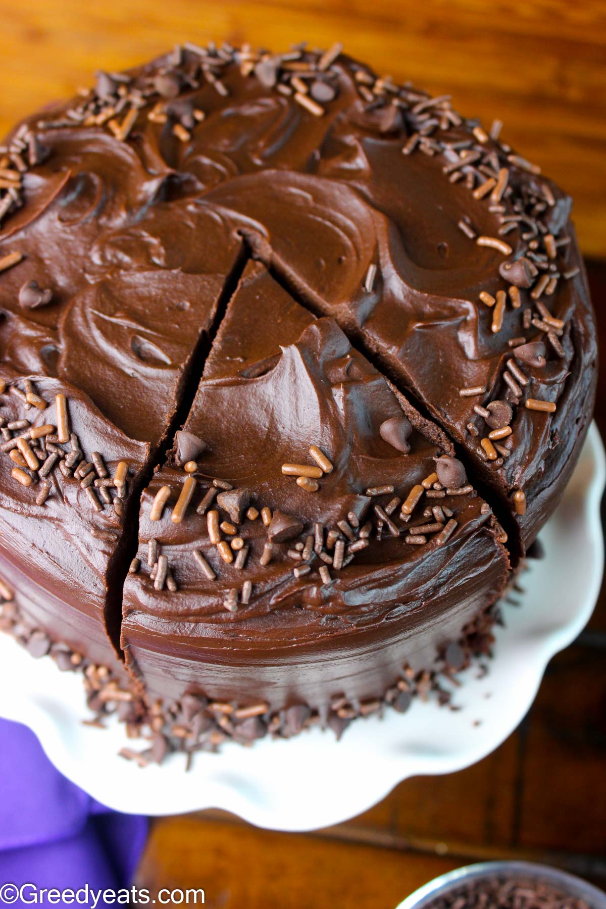 Soft and moist Chocolate cake covered in glossy Chocolate frosting on a white cake stand. 