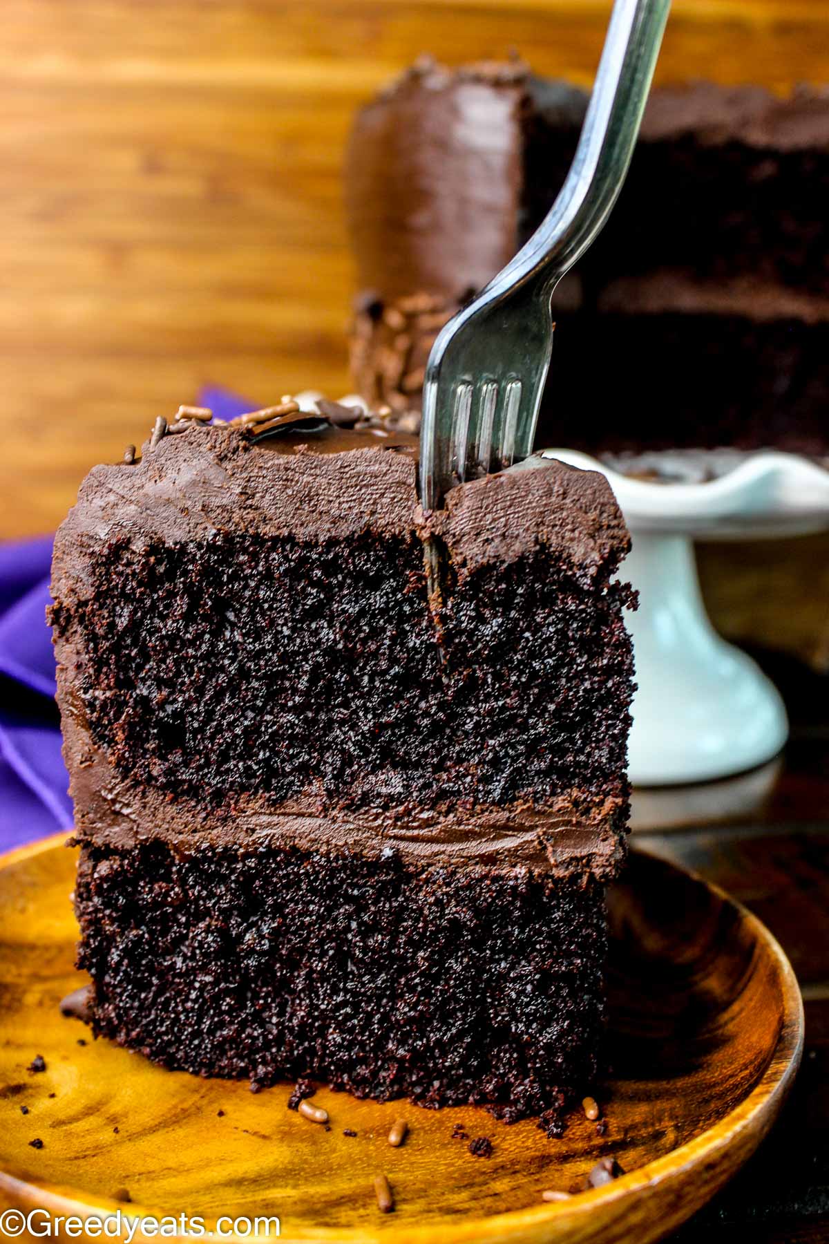 A Slice of one bowl chocolate cake topped with chocolate frosting kept on a wooden plate.