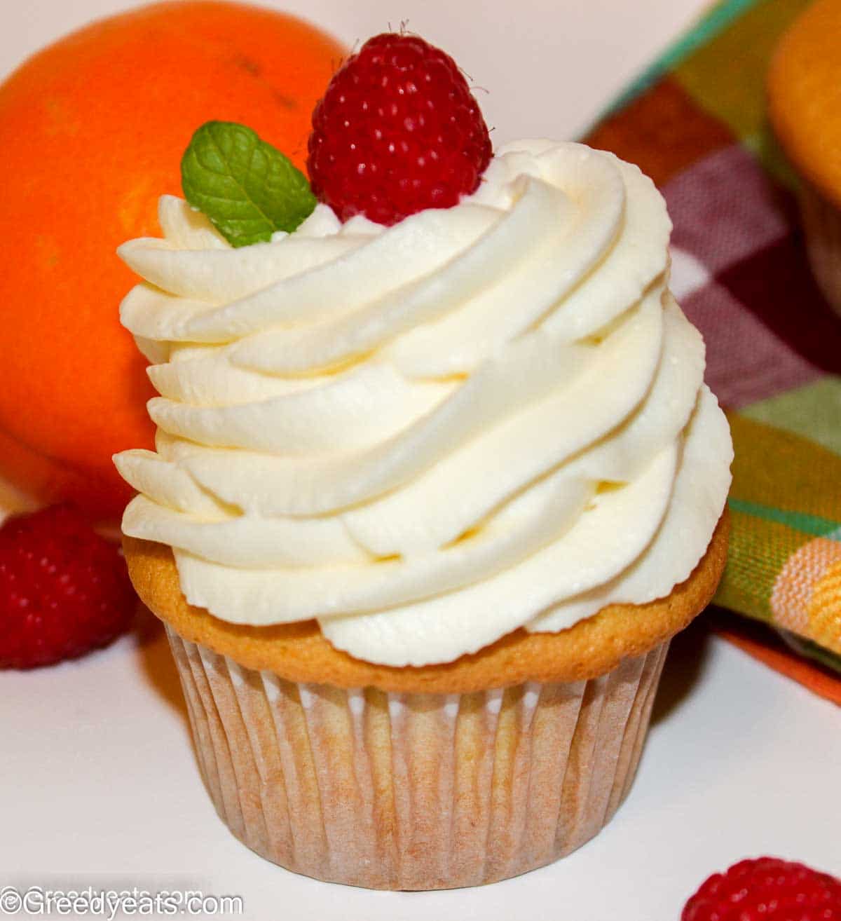 Orange Cupcake with piped orange buttercream frosting and a raspberry on top.
