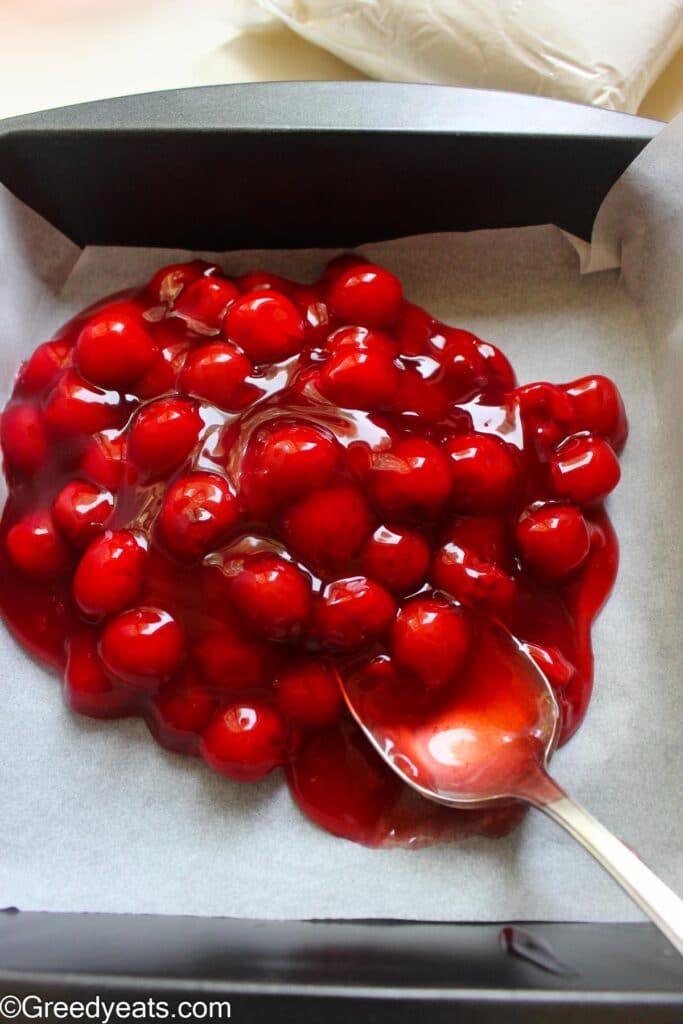 Spreading cherry filling in a lined/greased baking pan.