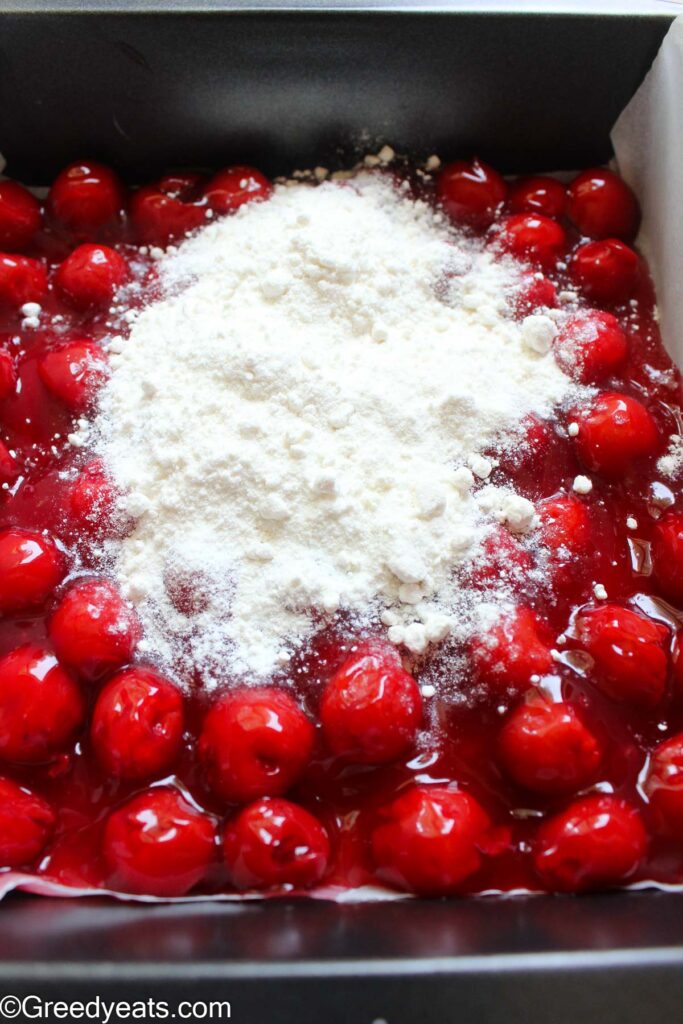Pouring and spreading yellow cake mix all over cherry filling.
