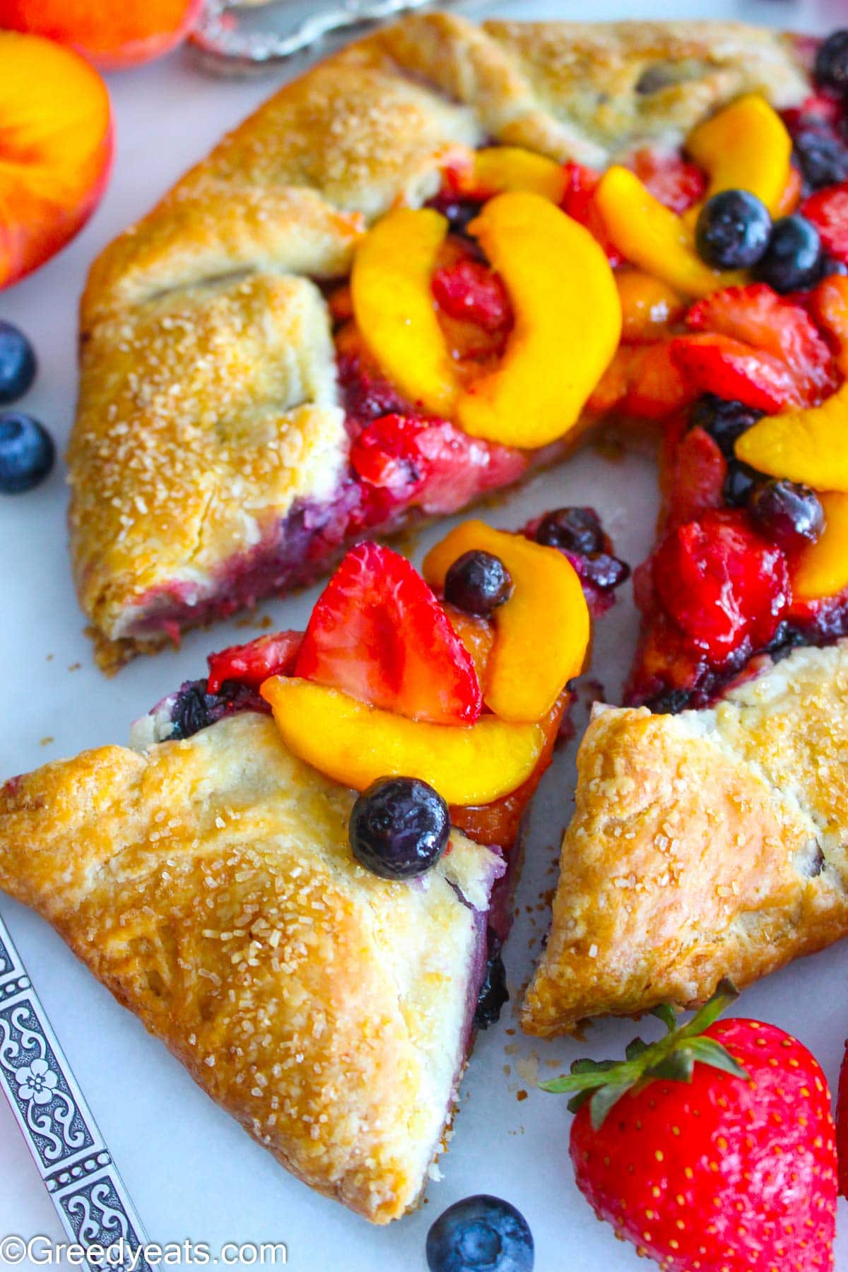 Buttery and flaky Peach Galette topped with coarse sugar and filled with berries filling.