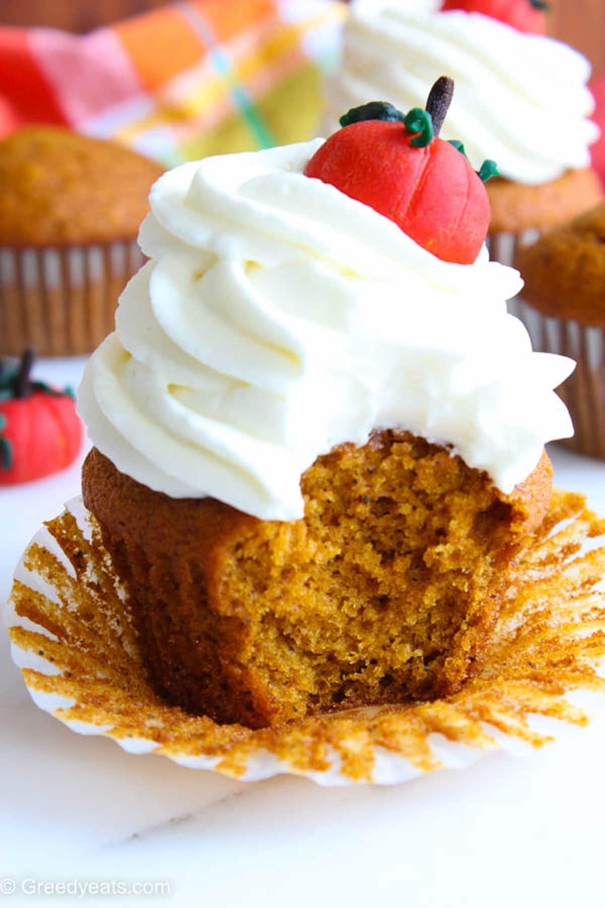 Pumpkin cupcake with creamy cream cheese frosting in a white cupcake liner. 