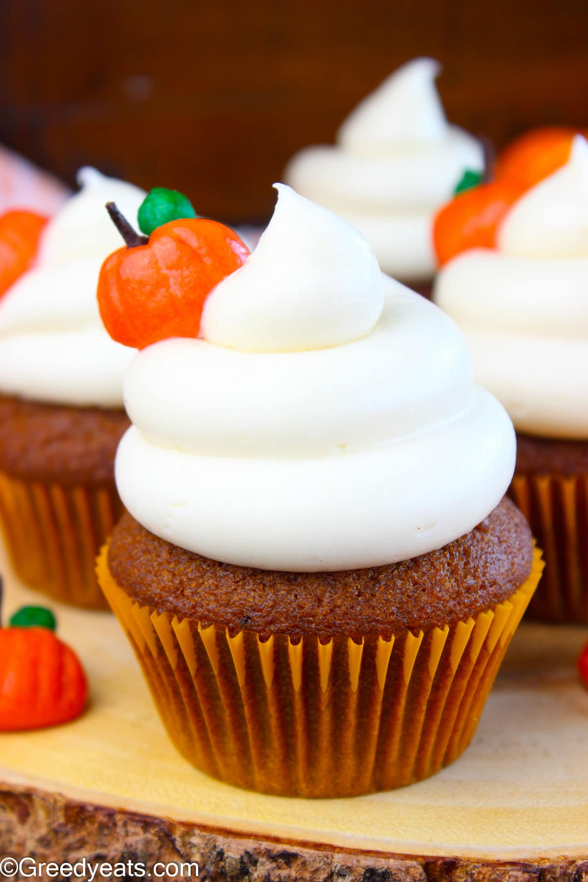 Pumpkin Cupcakes with cream cheese frosting topped with pumpkin toppers, kept on a wooden board.