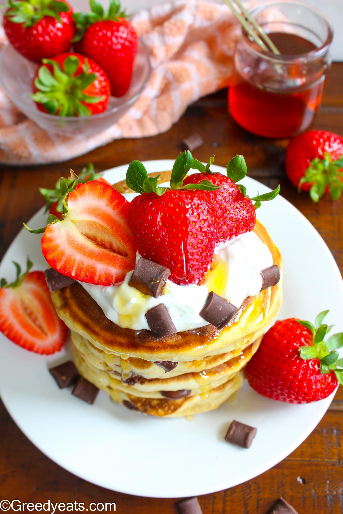 Pancakes with chocolate chunks, strawberries and fresh cream on a white plate.