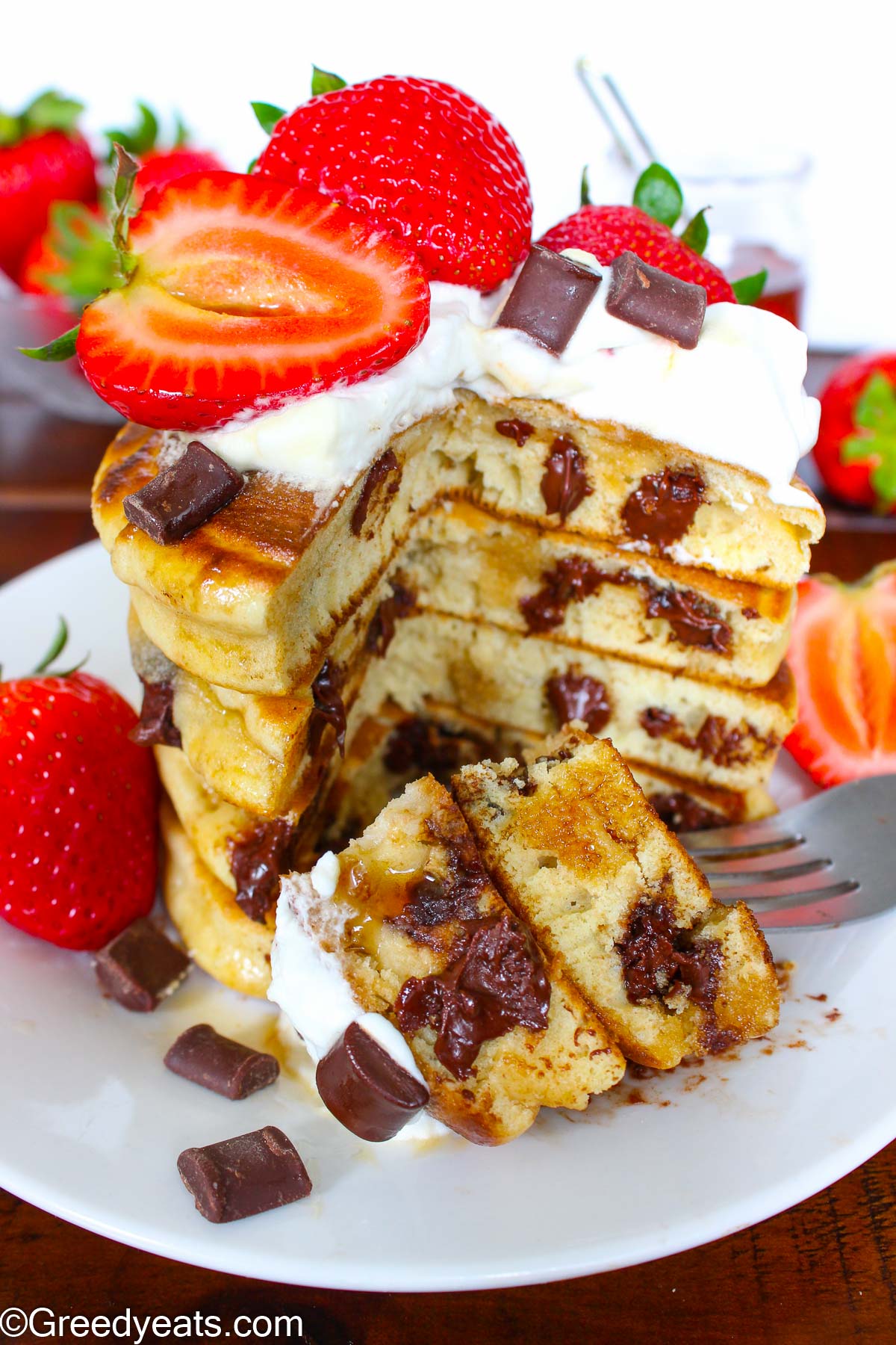 A stack of thick and fluffy chocolate chip pancakes with chocolate chunks and berries. 