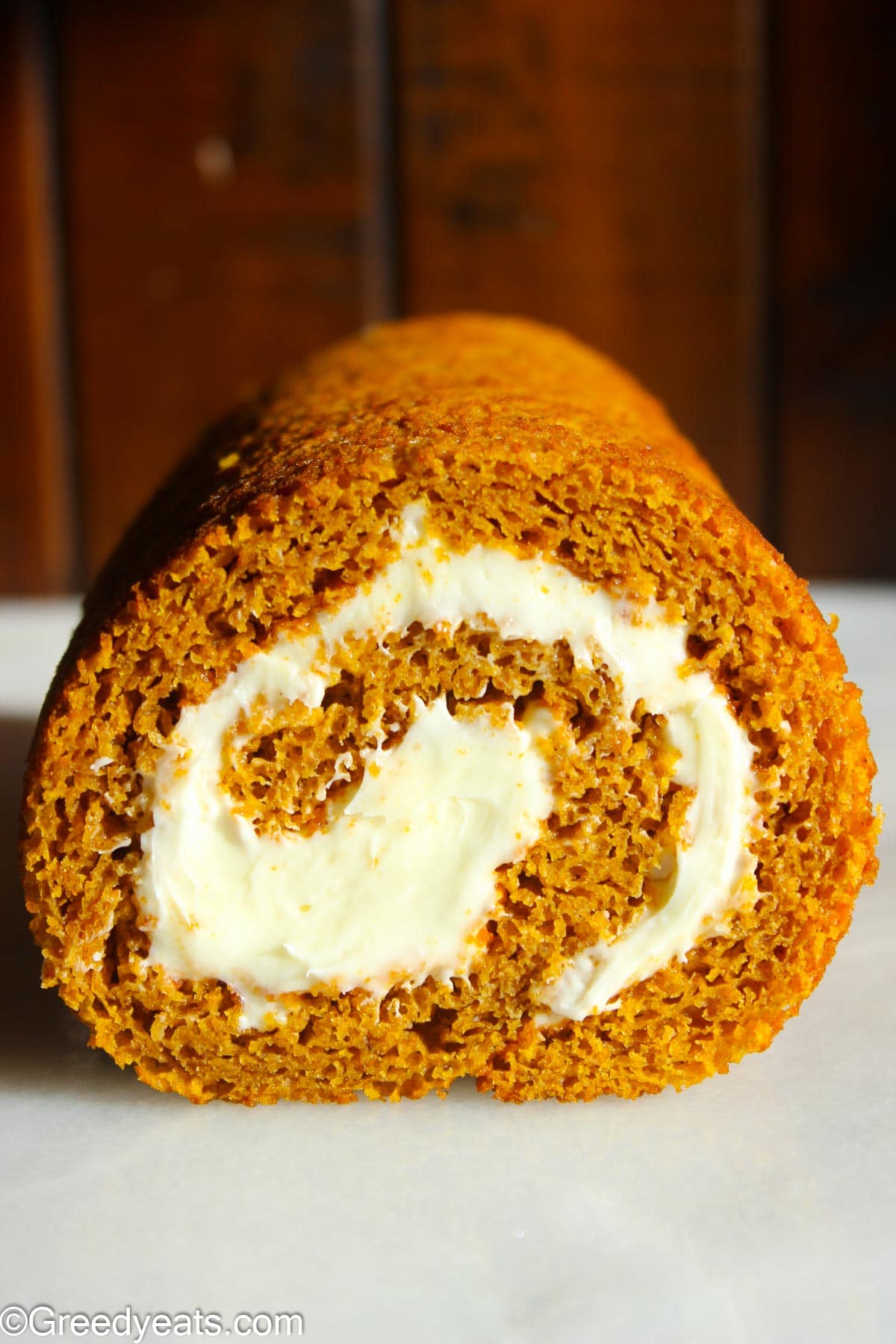 Pumpkin Cake roll with cream cheese filling ready to be served, kept on a marble slab.