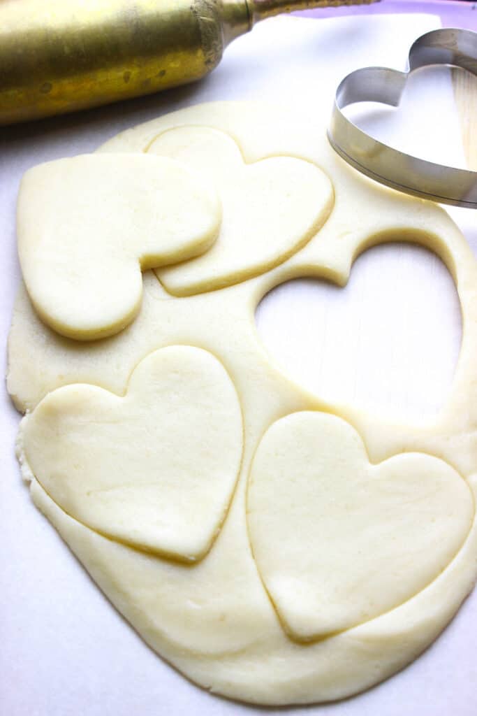Rolled out sugar cookie dough, cut into heart shapes for baking.