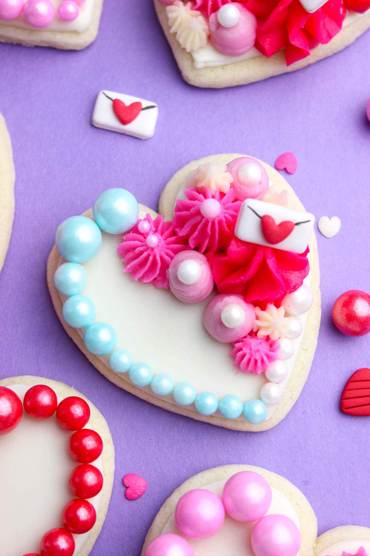 Heart sugar cookies topped with light pink and pink buttercream and blue valentines sprinkles.