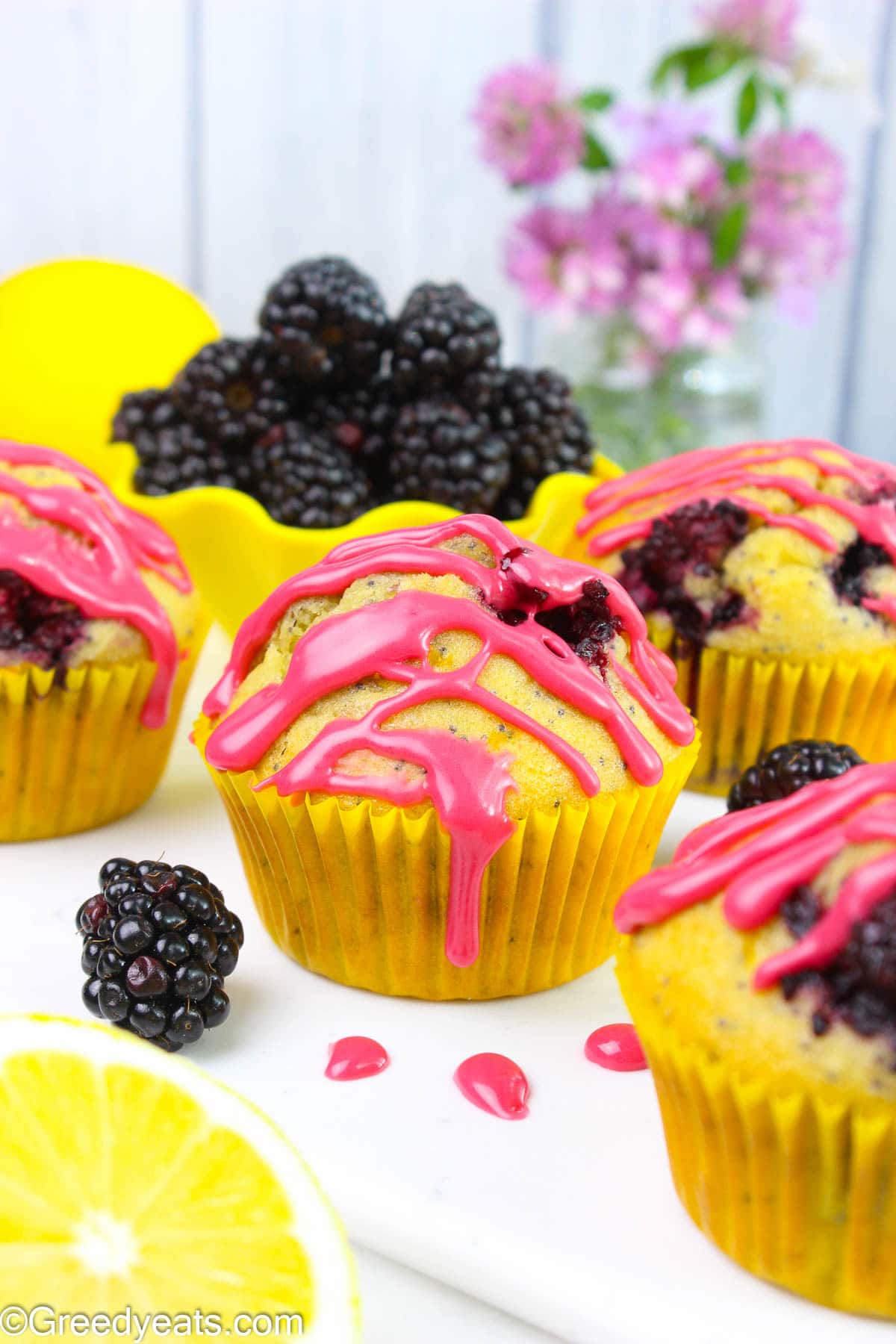 Easy Lemon blackberry muffins topped with sweet and fruity berry glaze in yellow cupcake liners.