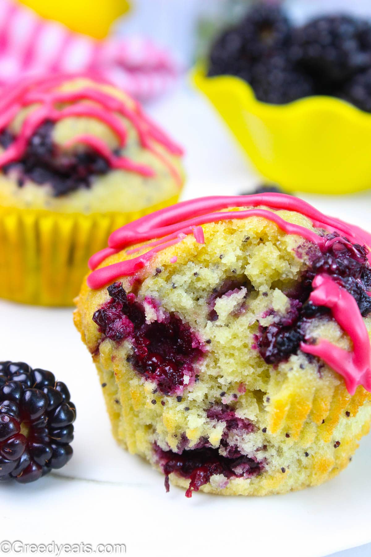 Tall, light and soft lemon poppyseed muffins dotted with blackberries and pink glaze.
