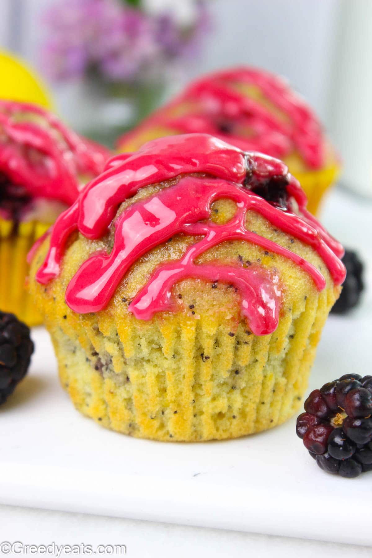 Thick and fruity berry glaze sitting on lemon muffins dotted with berries and poppyseeds.