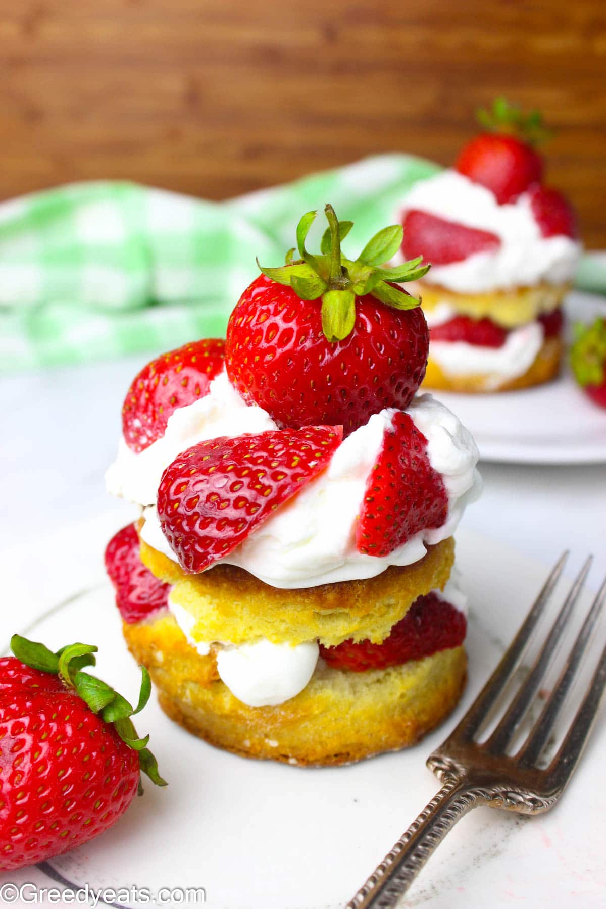 A layered shortcake biscuit with two layers of whipped cream topping and strawberries on a white plate.