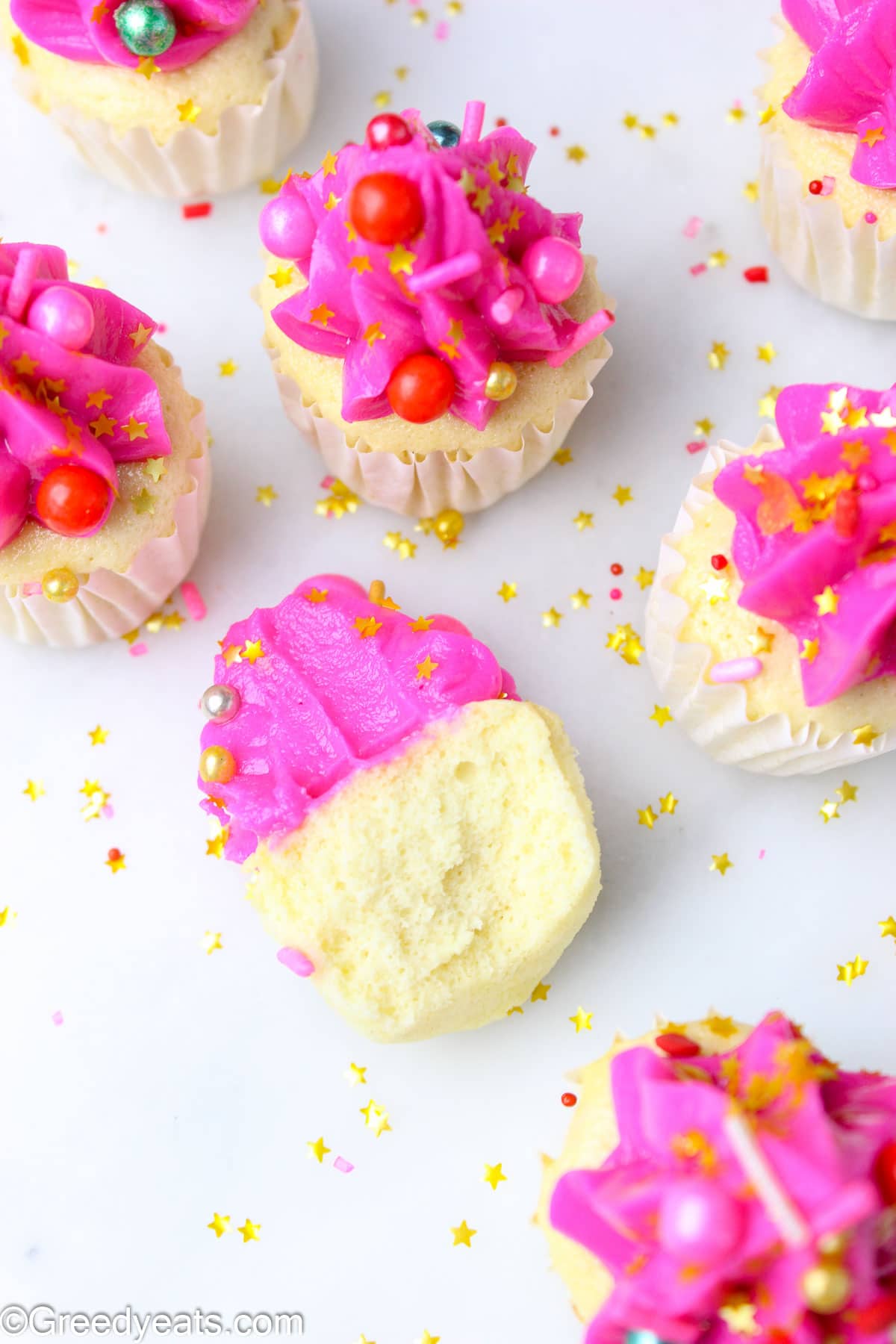 Moist and fluffy Mini Vanilla Cupcakes with pink buttercream and sprinkles on a white board.