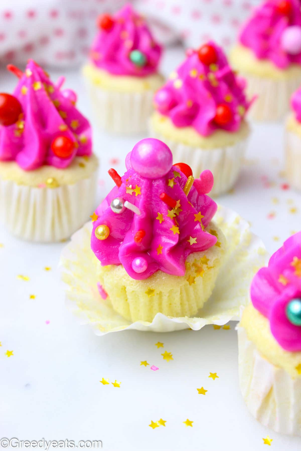 Mini Cupcakes topped with hot pink buttercream frosting and sprinkles in a white cupcake liner.