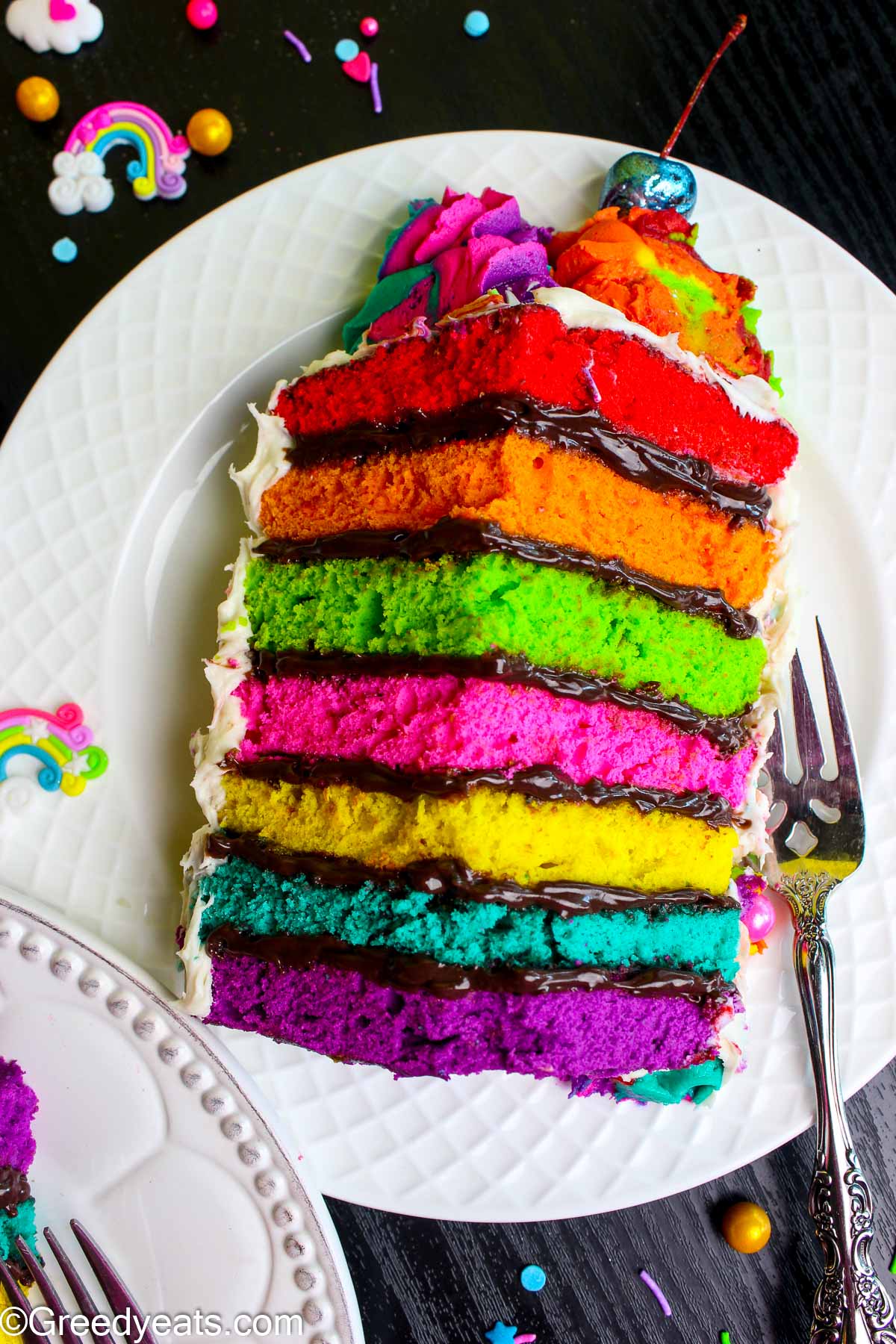 Soft and moist slice of Rainbow Cake filled with chocolate filling, topped with white buttercream and rainbow buttercream swirls.