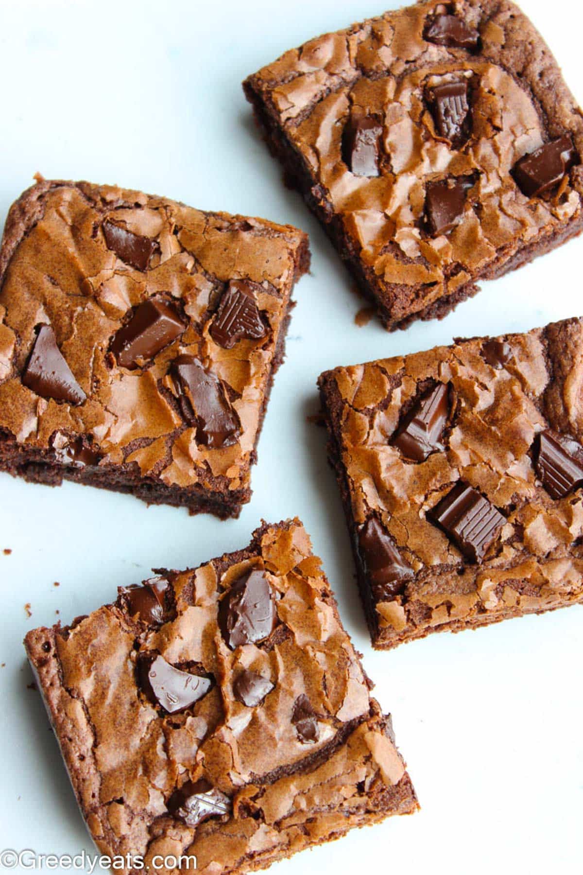 Crinkly, fudgy and chewy brownies topped with melty chocolate chunks on a white board.. 