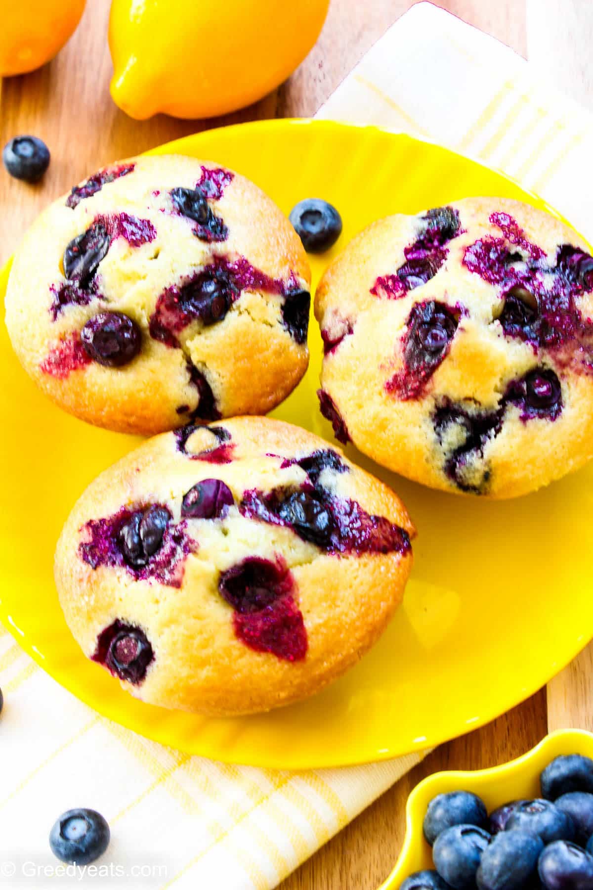 Super tall and shiny Lemon Berry Muffins made with yogurt served on a yellow plate.