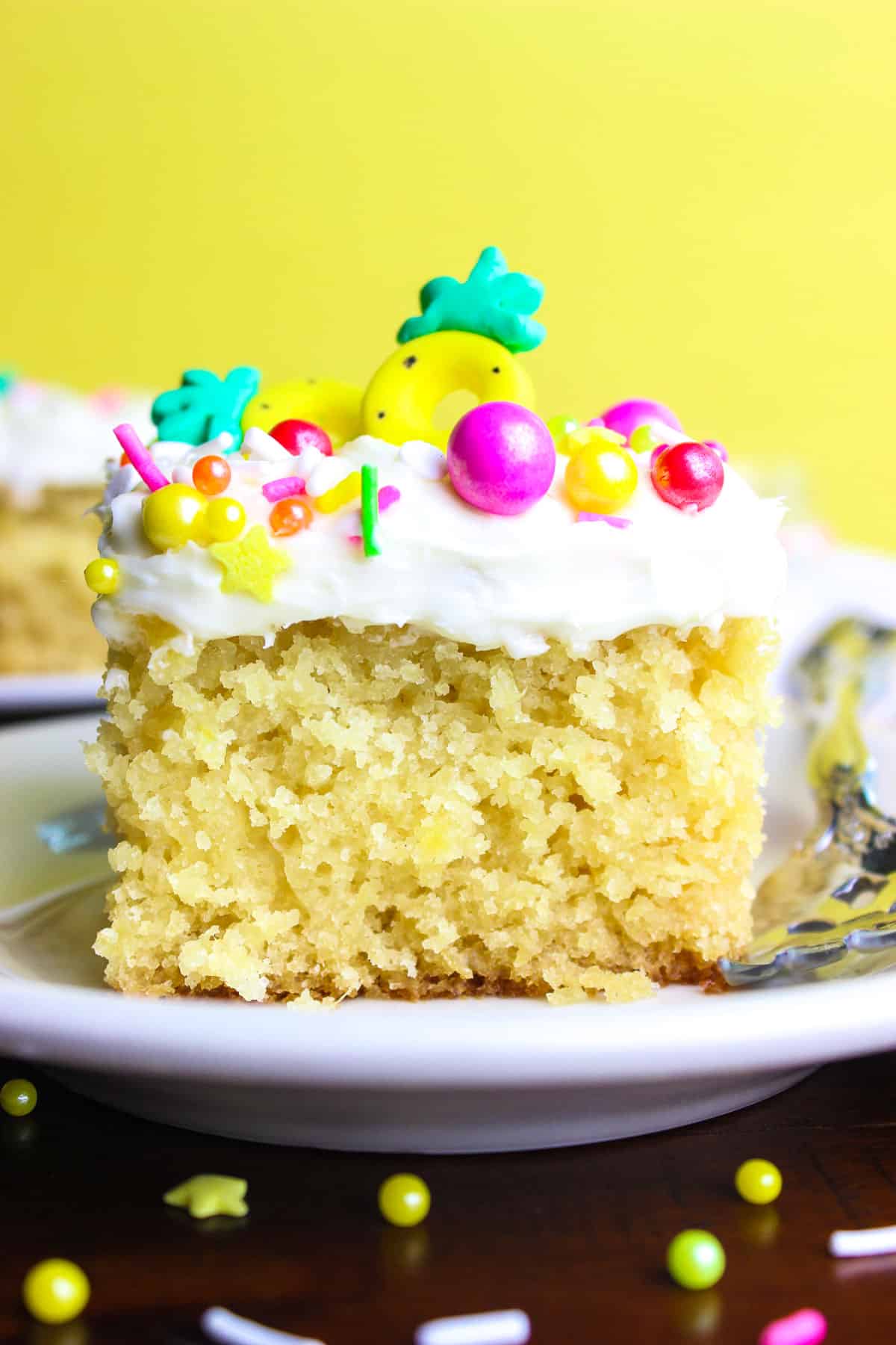 Pineapple cake slice topped with cream cheese frosting and sprinkles kept on a white plate.