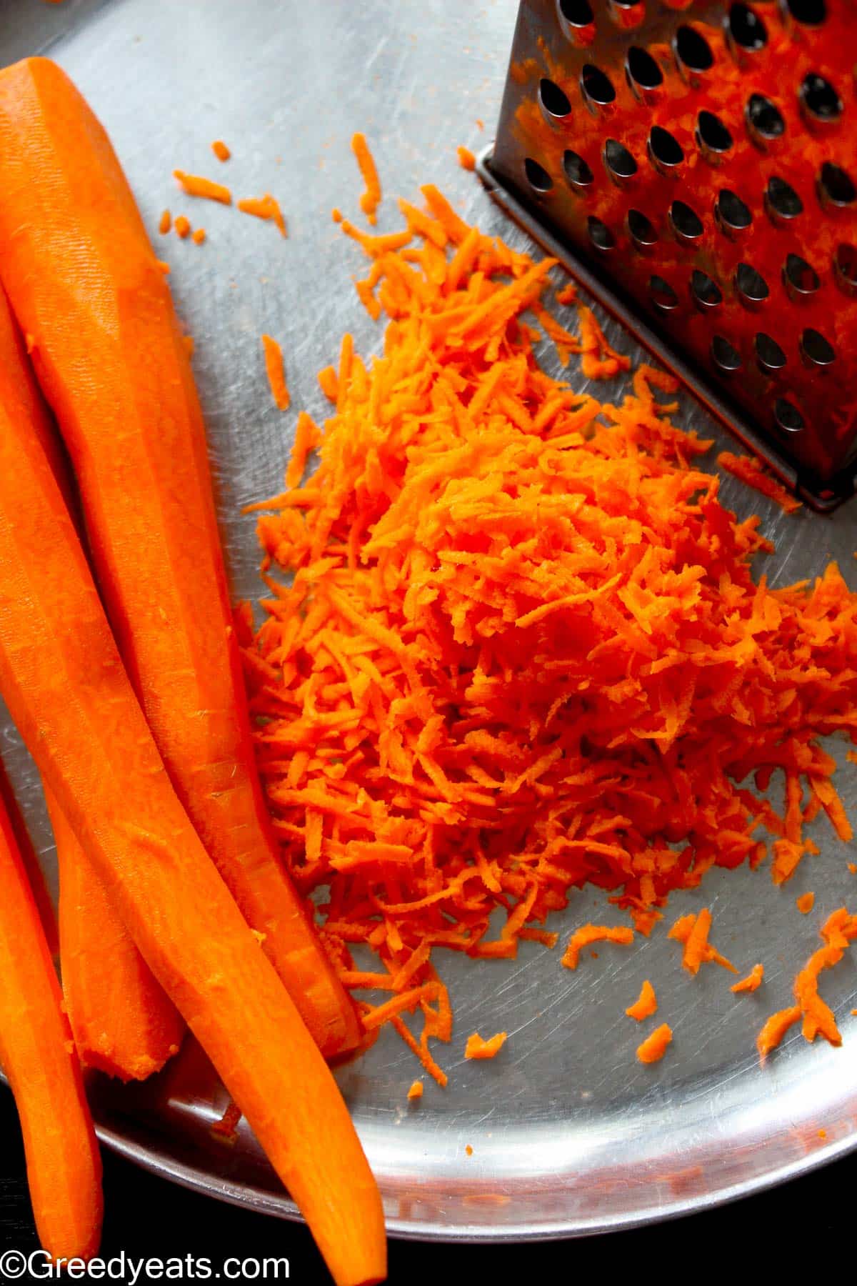 Peeled carrots getting grated with a box grater.