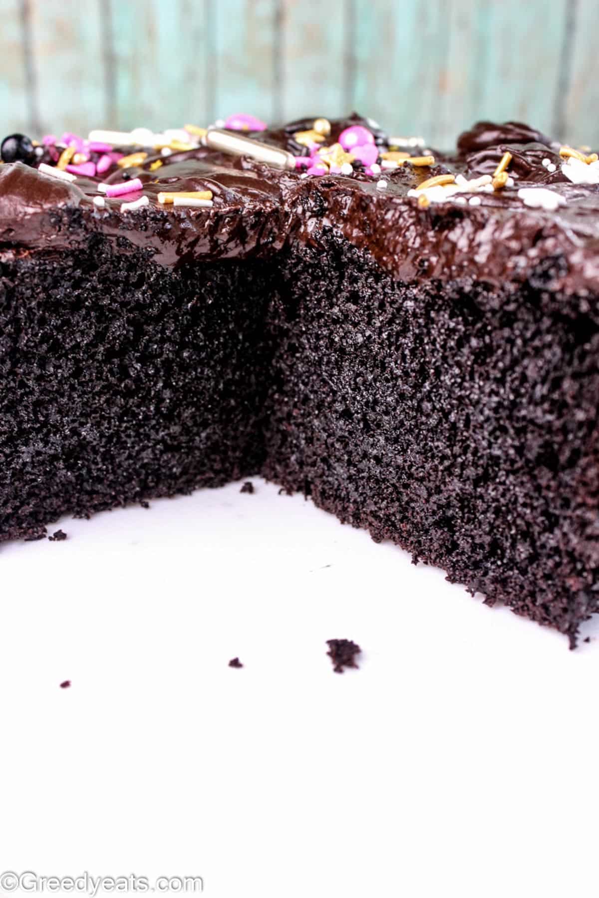A rich, fluffy and moist chocolate cake with ganache and sprinkles, kept on a white board.