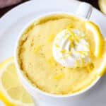 Lemon cake in a mug topped with whipped cream and lemon zest.