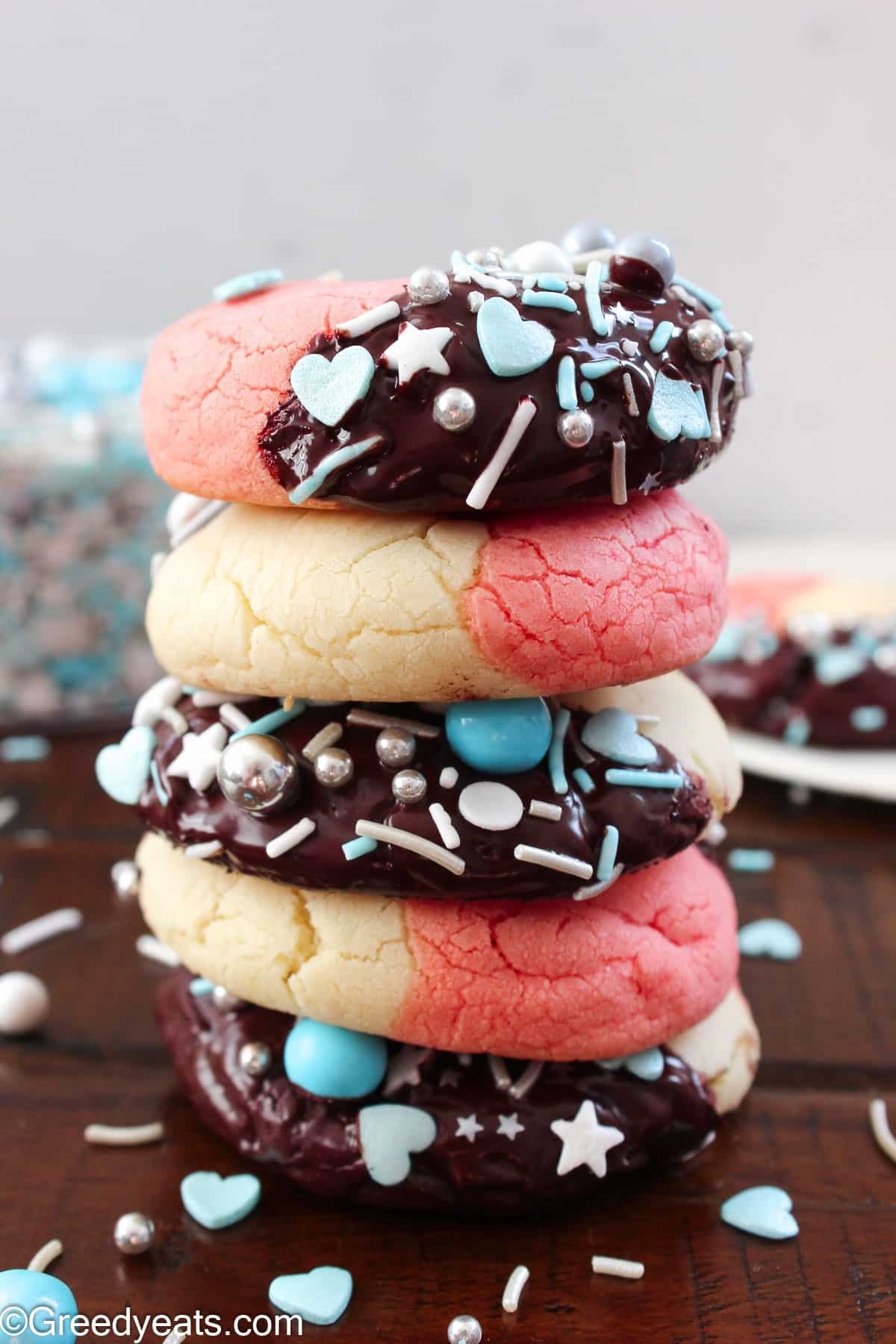A stack of thick, soft and puffy Neapolitan Cookies dunked in chocolate and topped with blue hearts sprinkles.