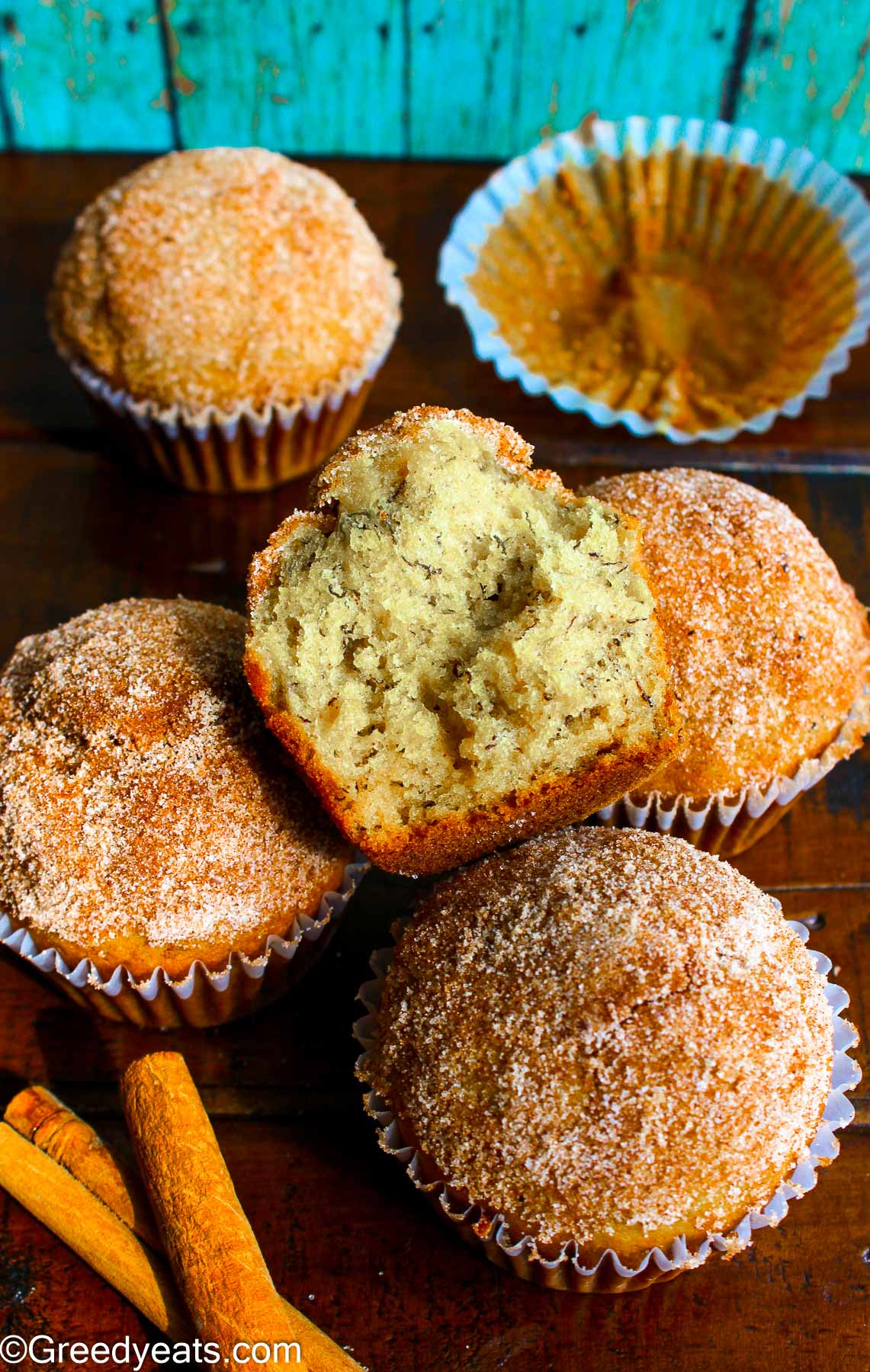 Half muffin kept in a muffin liner with more beautifully domed banana muffins in the background.