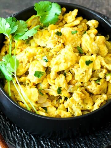 Soft, flavor packed and juicy egg bhurji topped with coriander served in a black bowl.